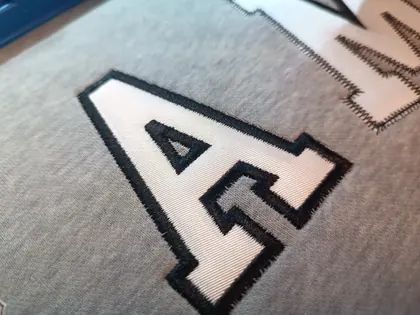 Gros plan de lettres A et M en appliqué avec contour brodé.