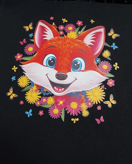Transfert DTF pressé sur un vêtement noir : une tête de renard souriante entourée de fleurs et de papillons, aux couleurs franches.