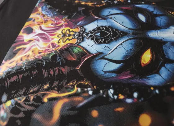 Agrandissement d’un transfert DTF pressé sur un chandail noir : un masque bleu craquelé et des flammes orangées, l’armure du tissu visible sous l’encre.